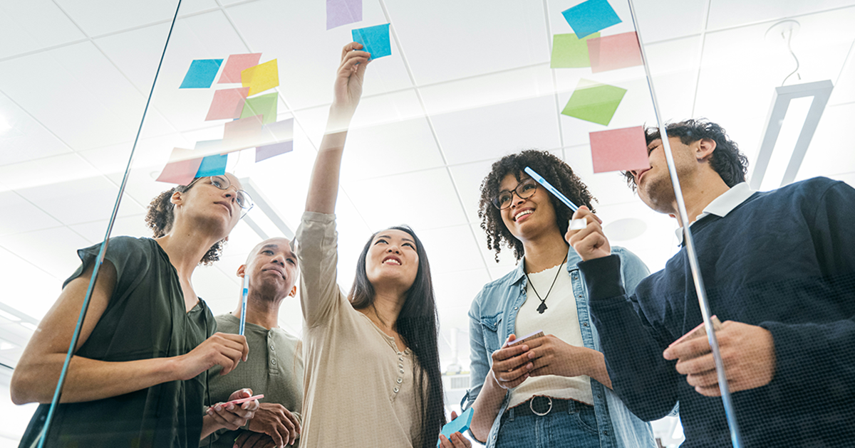 Diverse group of people in an office, planning on a glass wall with colorful sticky notes.